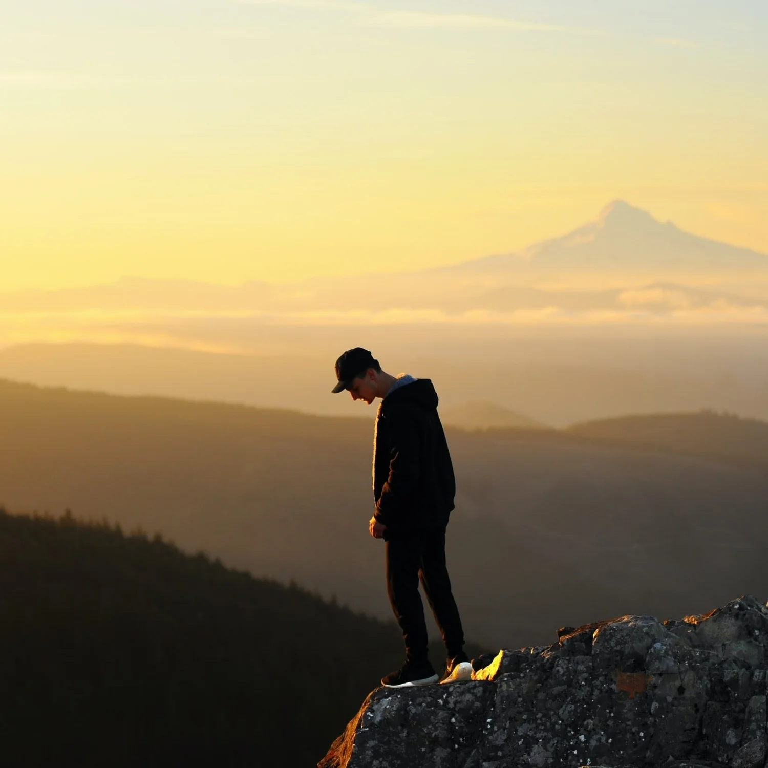 Man standing on a cliff overlooking mountains at sunset
